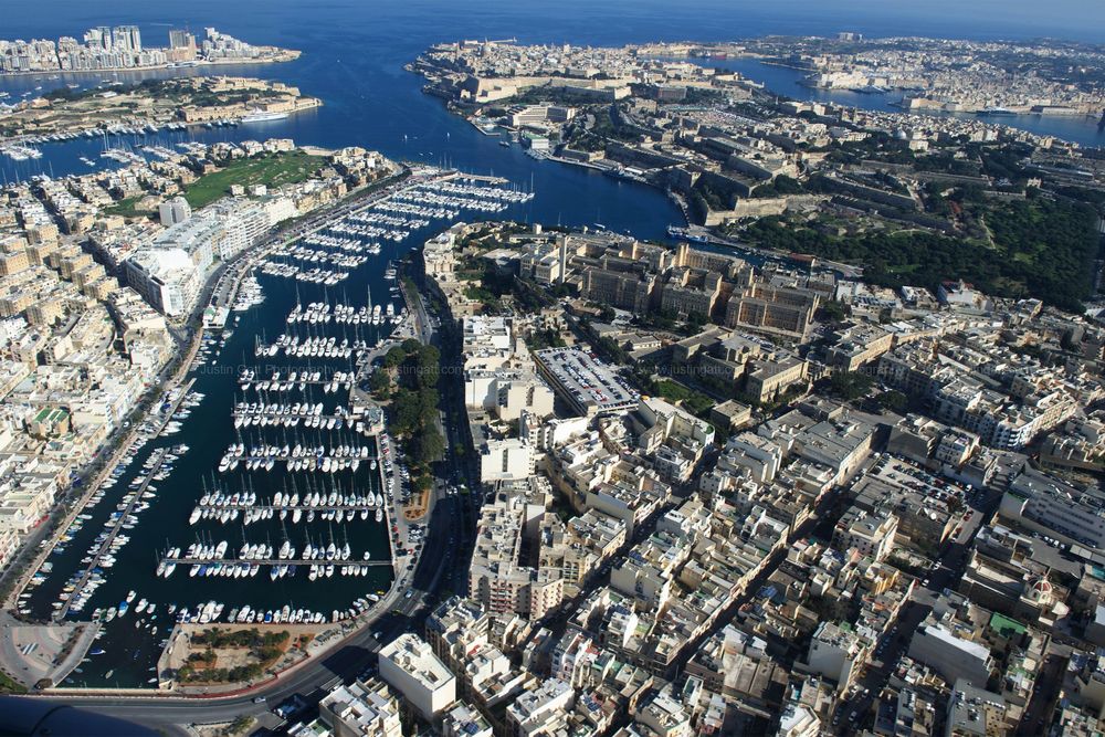 Aerial view of a large marina filled with boats surrounded by dense urban development in Malta.