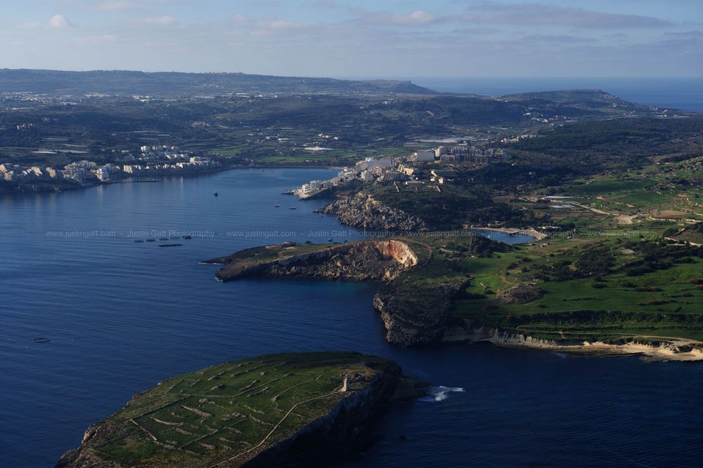 Coastal landscape showing rugged cliffs and green fields meeting the deep blue Mediterranean Sea.