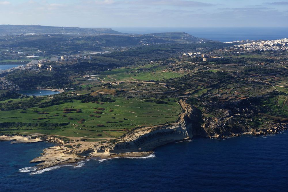 Scenic coastline view with rolling hills, scattered settlements and dramatic cliff formations.