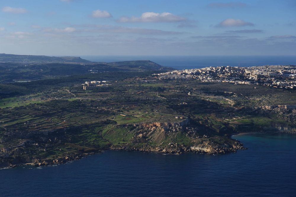 Panoramic view of Malta's rocky coastline with urban development visible in the distance.