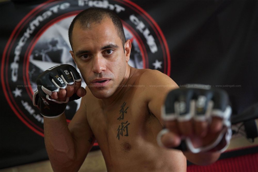 Mixed martial arts fighter in training gear poses in a fighting stance at a gym.