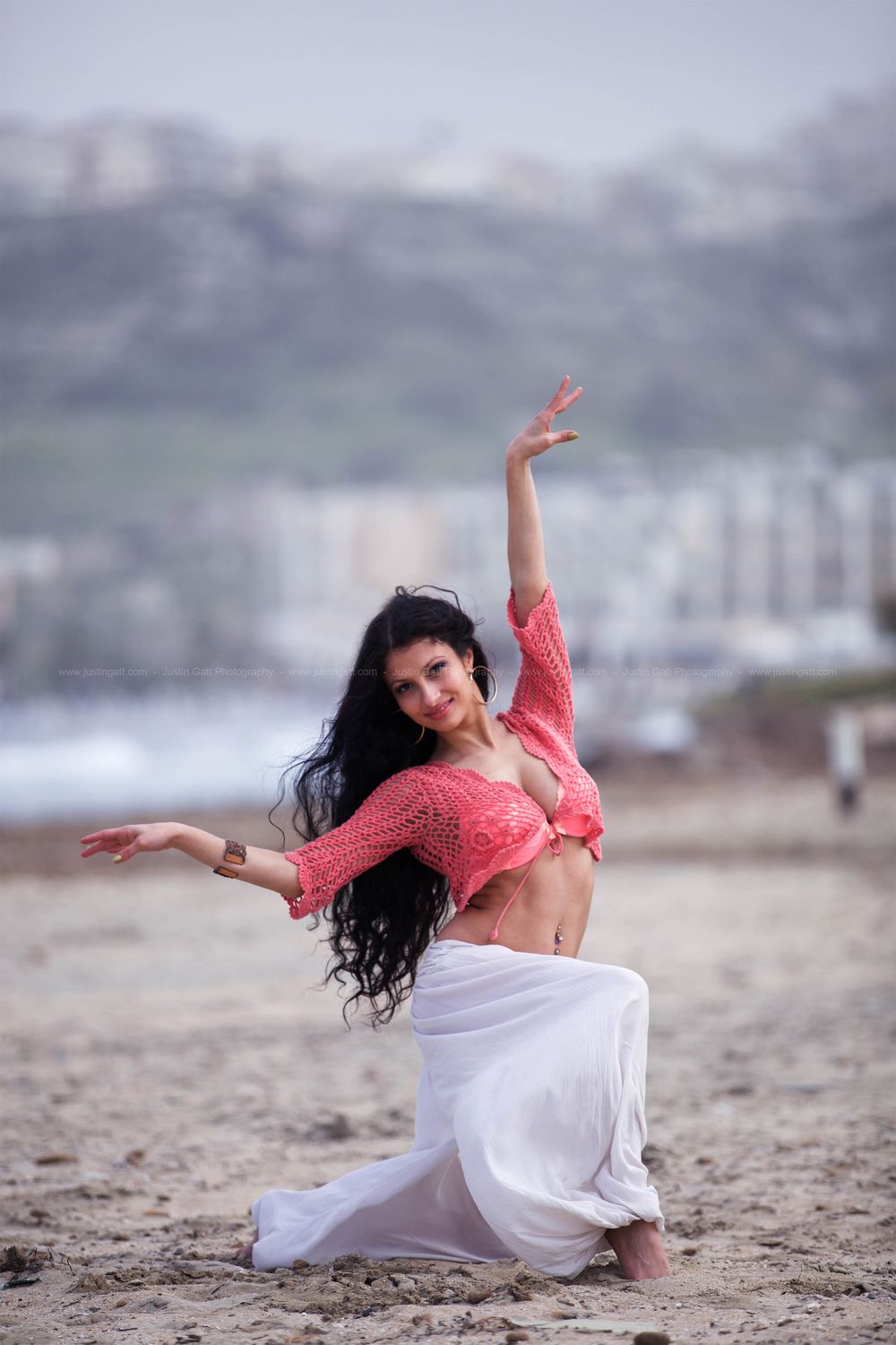 Dancer in white dress performs graceful movements on a sandy beach at dusk.