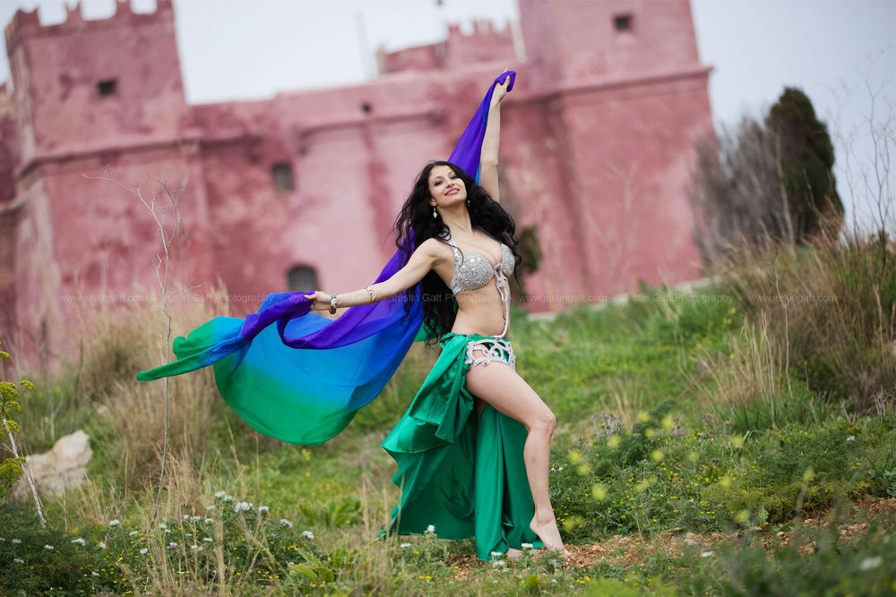 Flowing colorful dresses create movement against a pink castle backdrop in an artistic photoshoot.