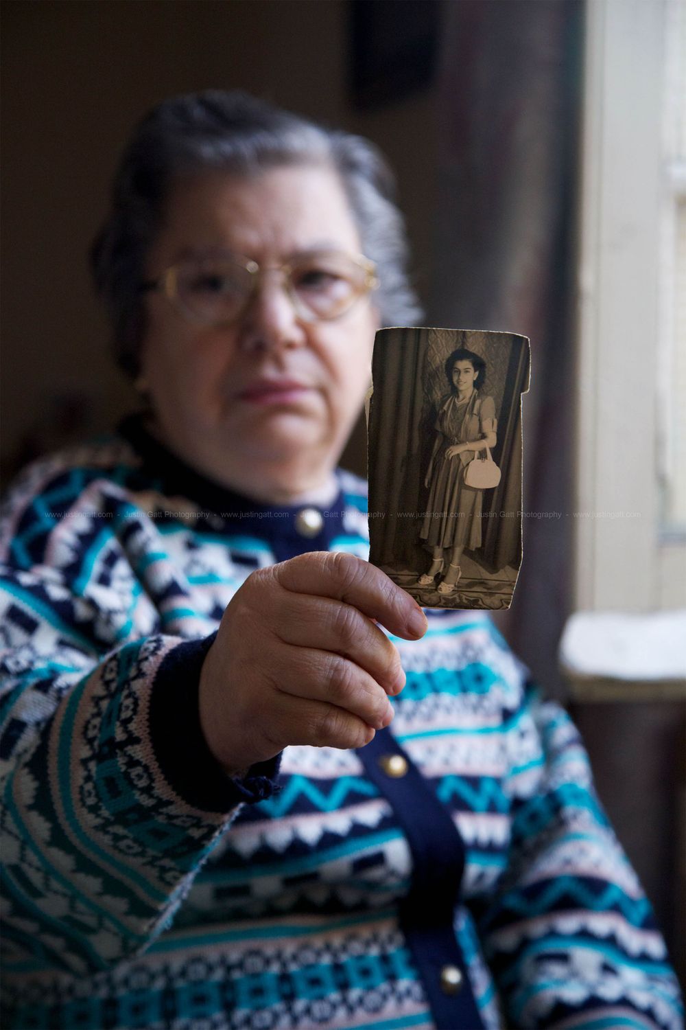 Person in festive sweater holds up vintage photographs while sitting indoors.
