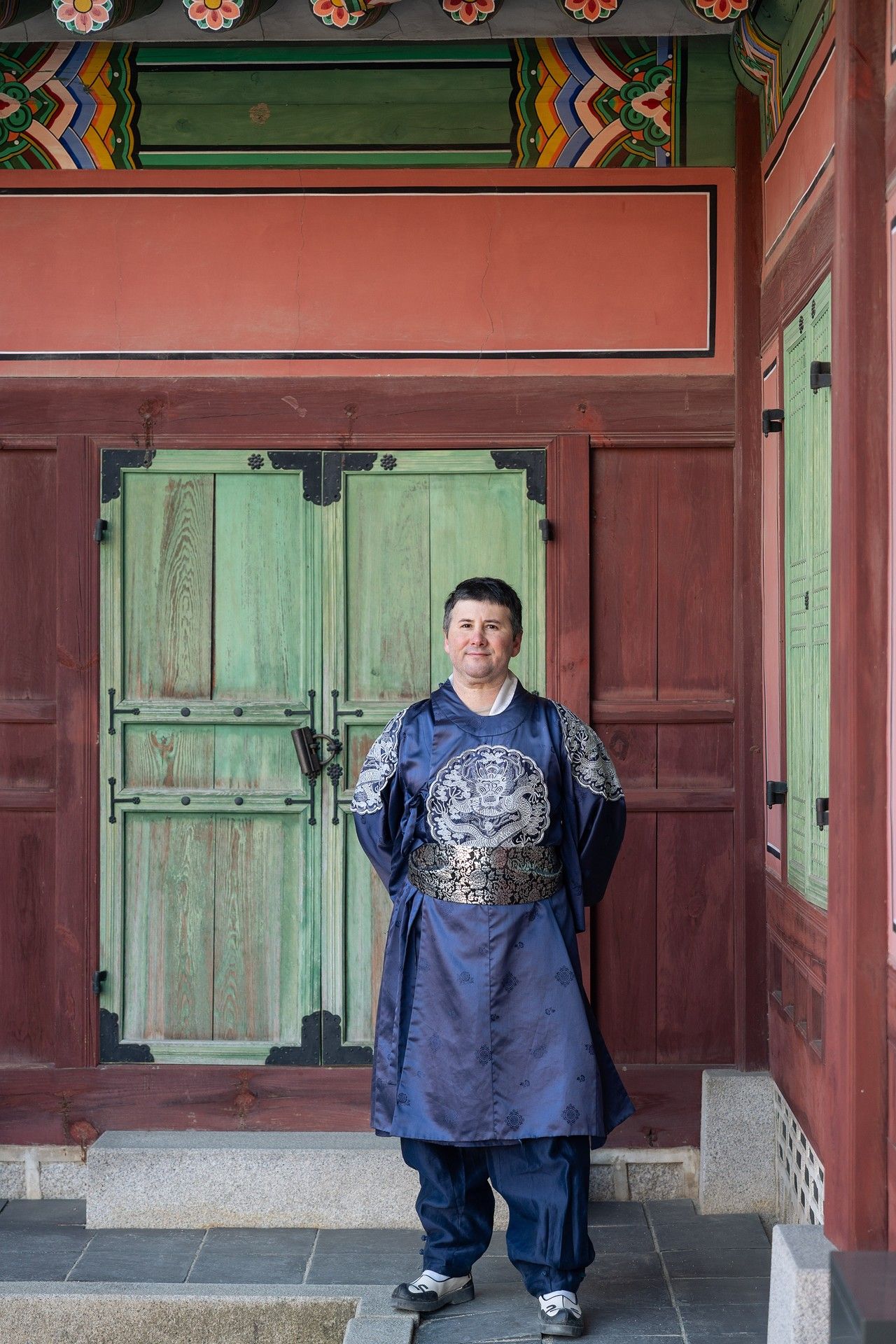 Five sequential photos of someone wearing a navy blue t-shirt standing in front of traditional Korean temple doors.