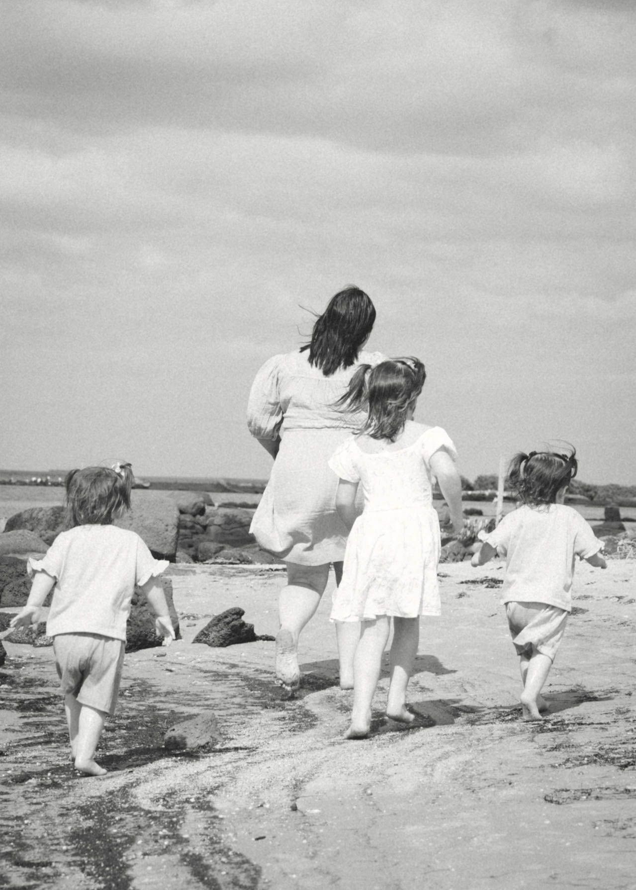 A vintage black and white photograph shows a group walking together along a beach path on a cloudy day.