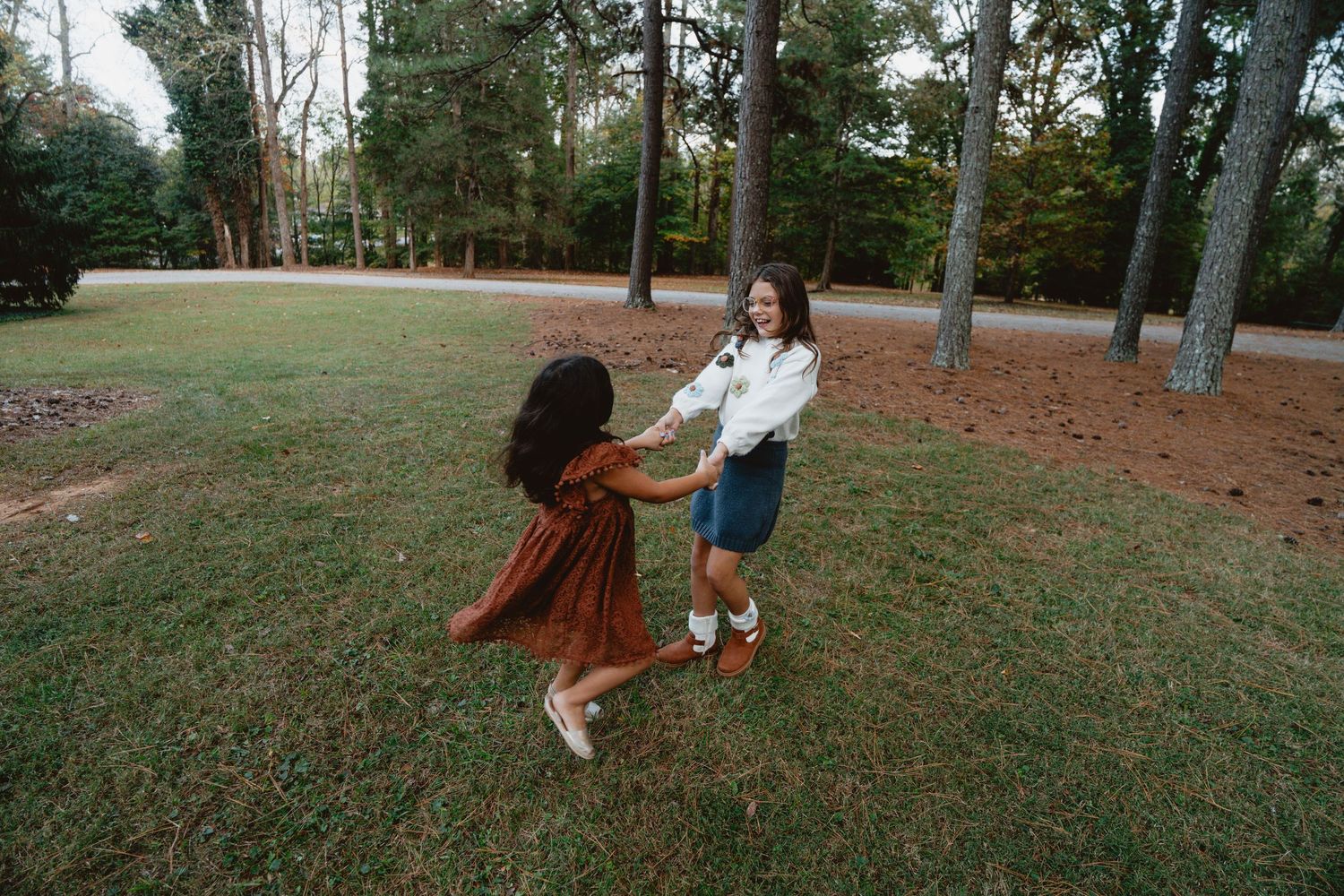 People playing on a grassy lawn with autumn trees in the background during a fall day.