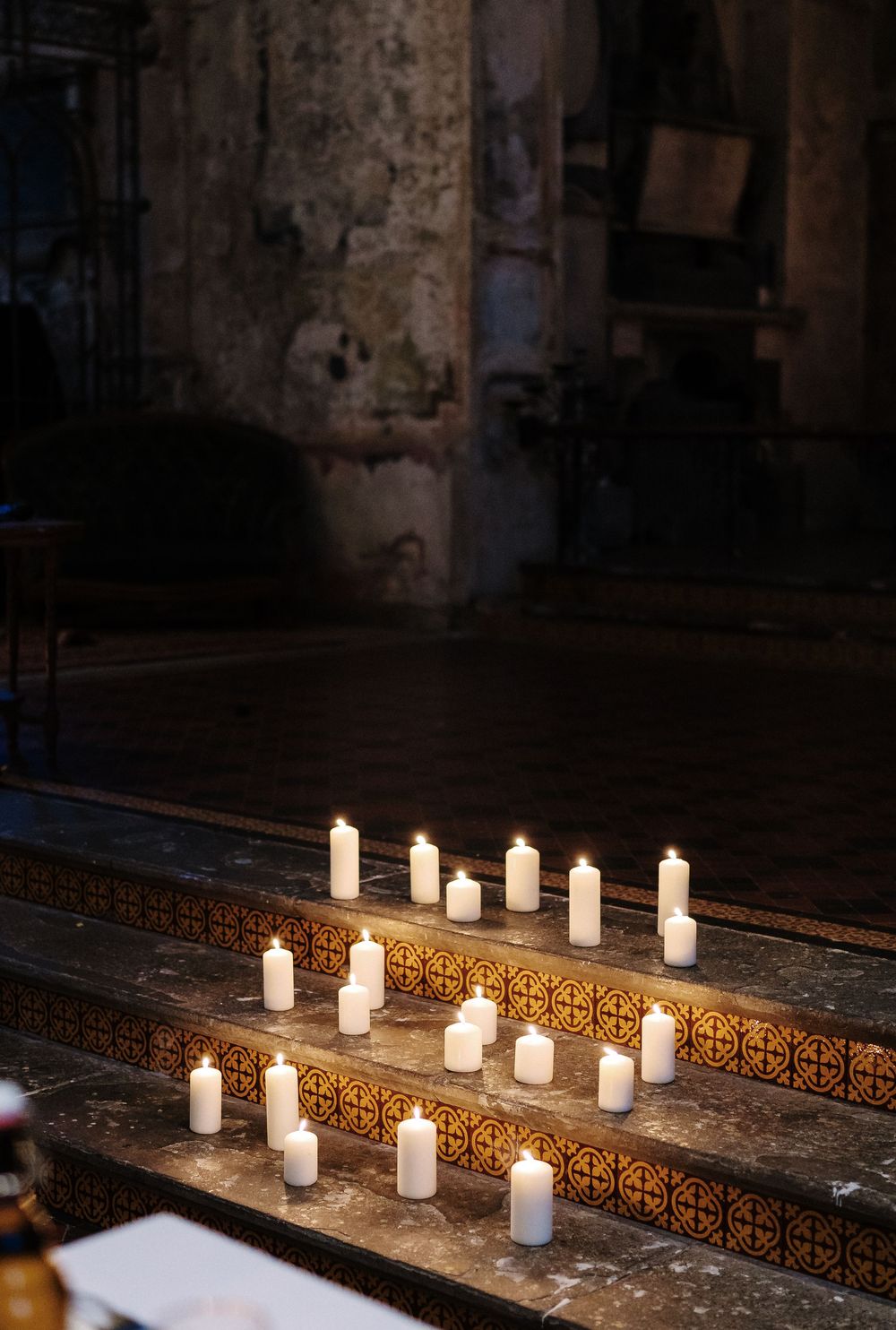 A row of white candles illuminating a dark rustic surface with ornate metalwork details.