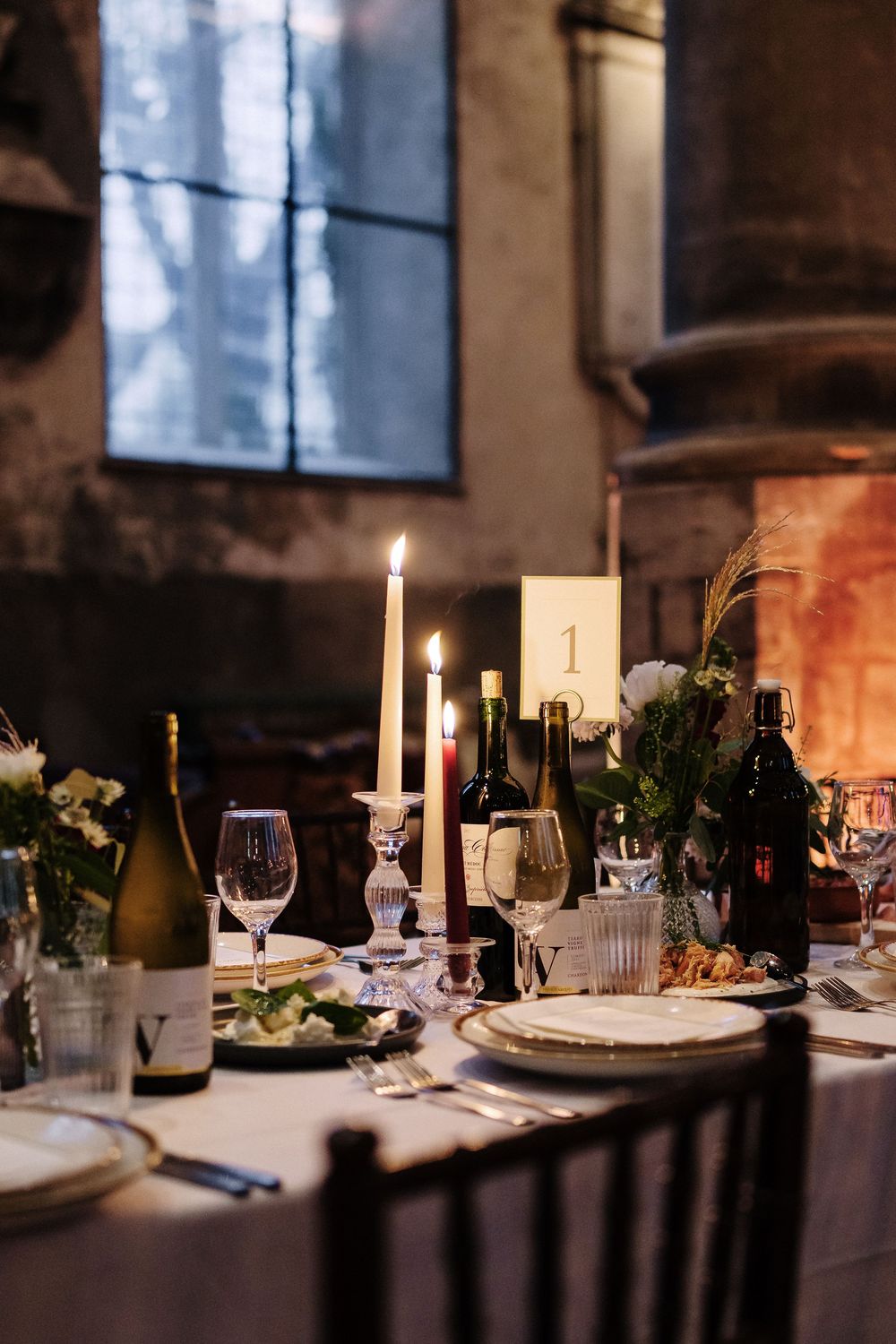Elegant wedding table setting with candles, greenery, and place settings in a rustic venue.