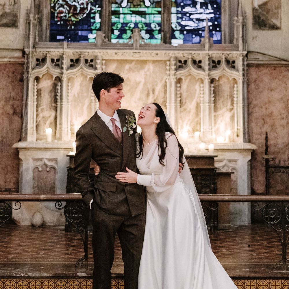 Wedding couple poses in front of ornate stained glass windows in a gothic church setting.