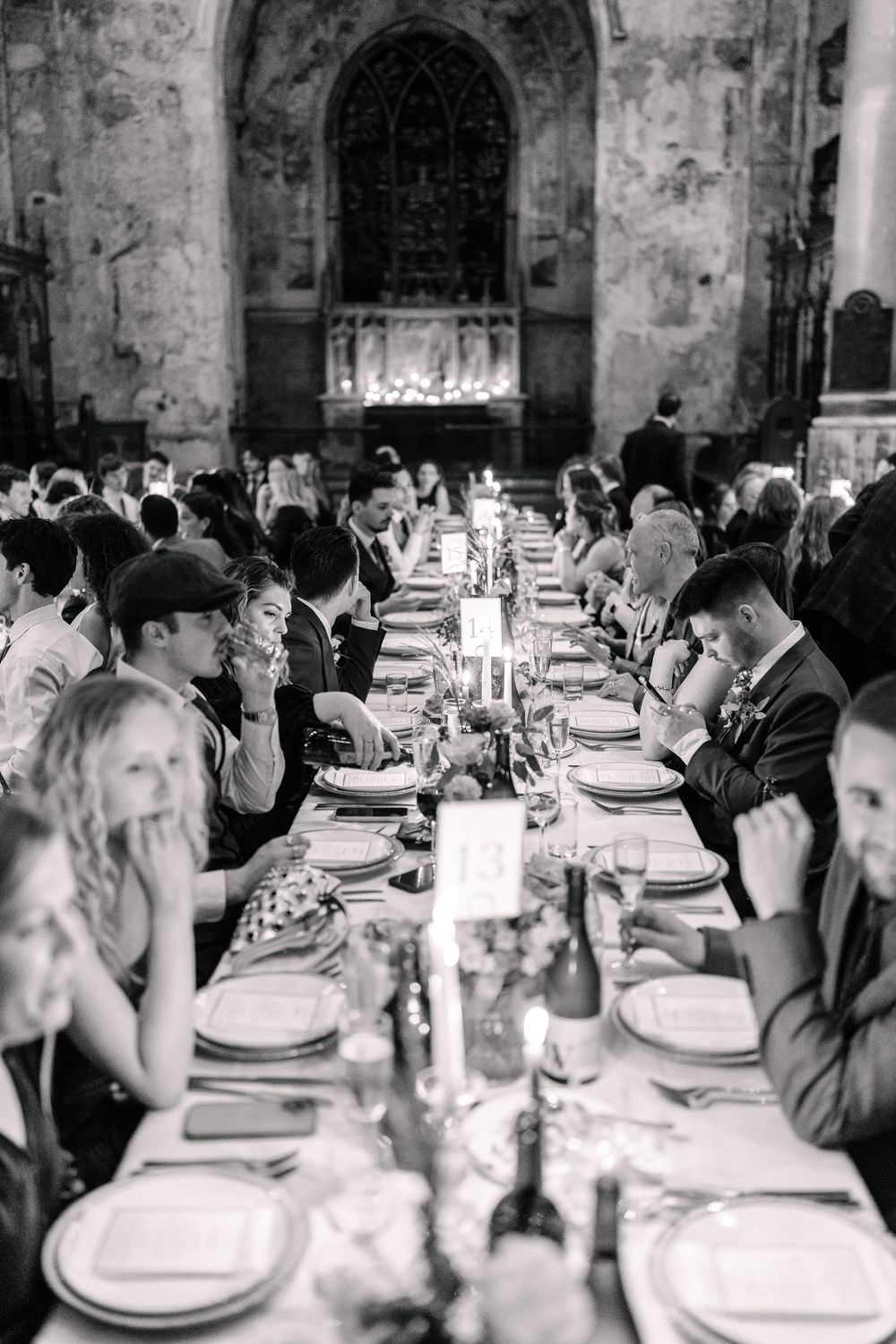 A long banquet table set for dinner with glowing candles and place settings in a rustic stone venue.