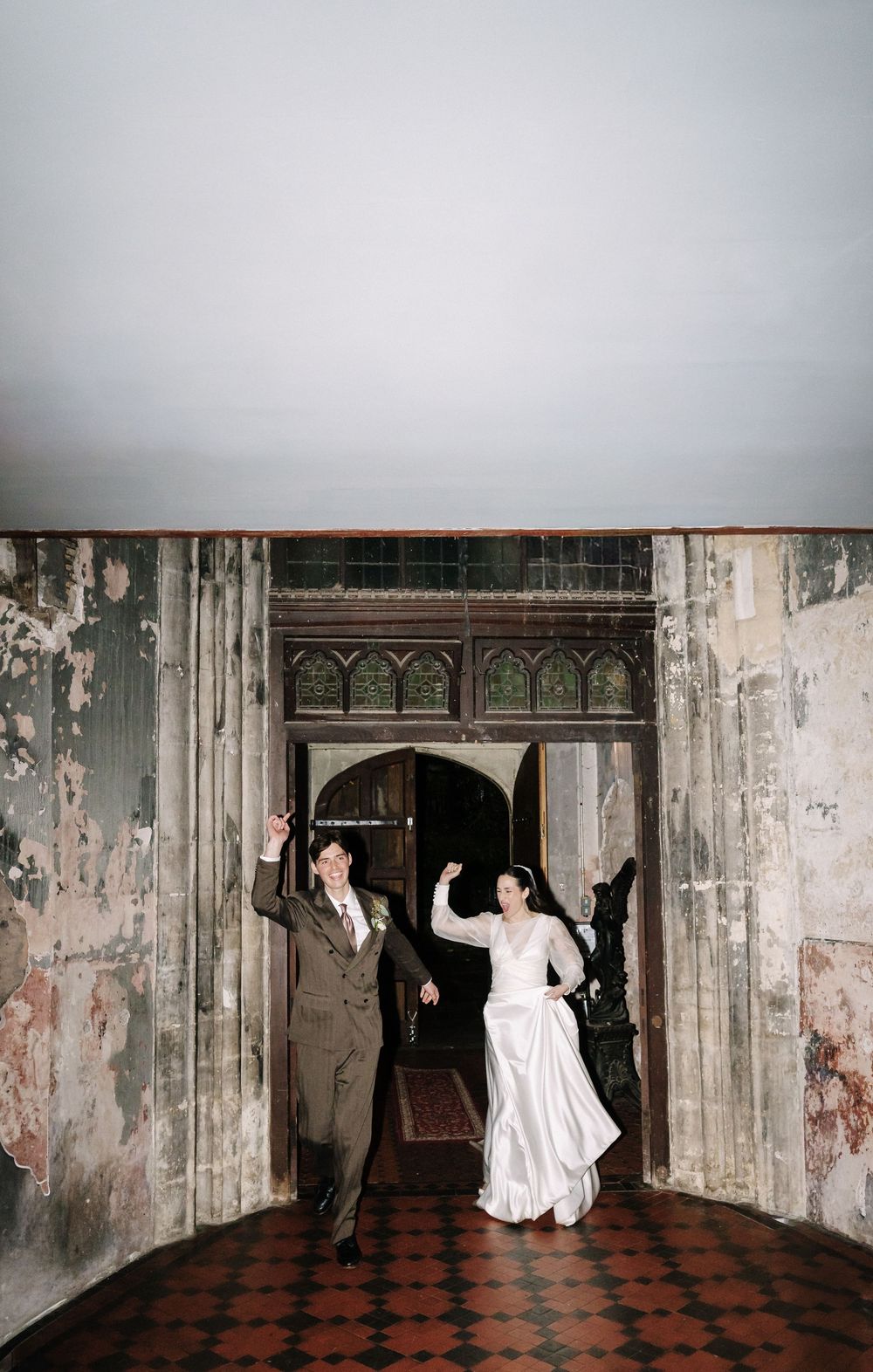 A couple joyfully exits through vintage weathered doors with peeling paint and ornate architectural details.