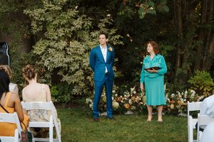 Wedding guests seated in white chairs on a lawn during an outdoor ceremony with trees in the background.