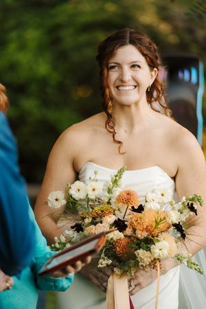 A bride holds a beautiful bouquet of peach and white flowers during an outdoor wedding ceremony.