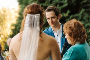 A couple in wedding attire stands together during a golden hour outdoor ceremony.
