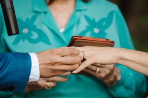 Close-up shot of hands during a wedding ceremony as a ring is placed on a finger against a turquoise background.