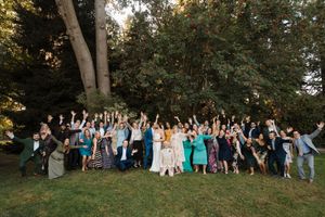 Large group of wedding guests pose together in a scenic outdoor garden setting at sunset.