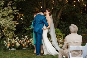 A wedding couple dances together in a lush garden setting during their outdoor reception celebration.