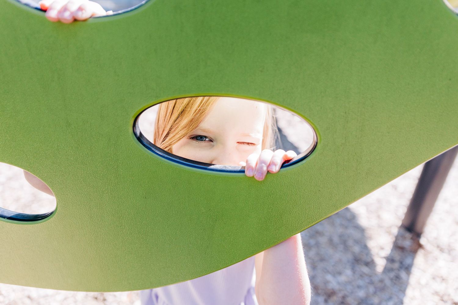 A young girl playfully peeks through a play set in Charlotte park.