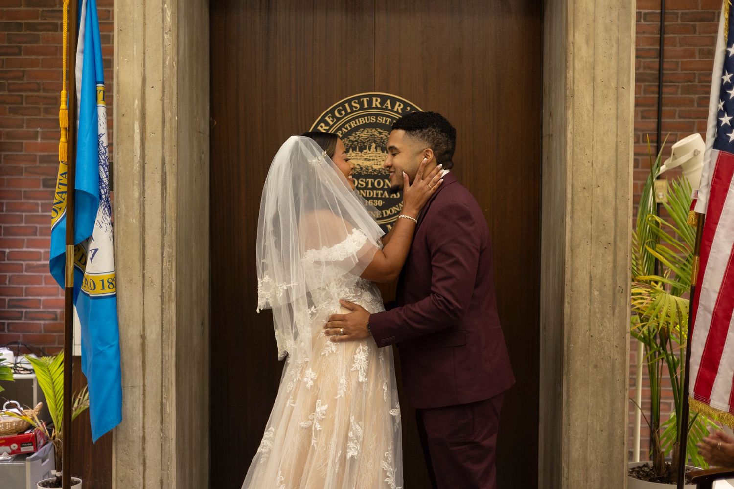 A couple stands at the altar during their wedding ceremony with flags and decorative elements in the background.