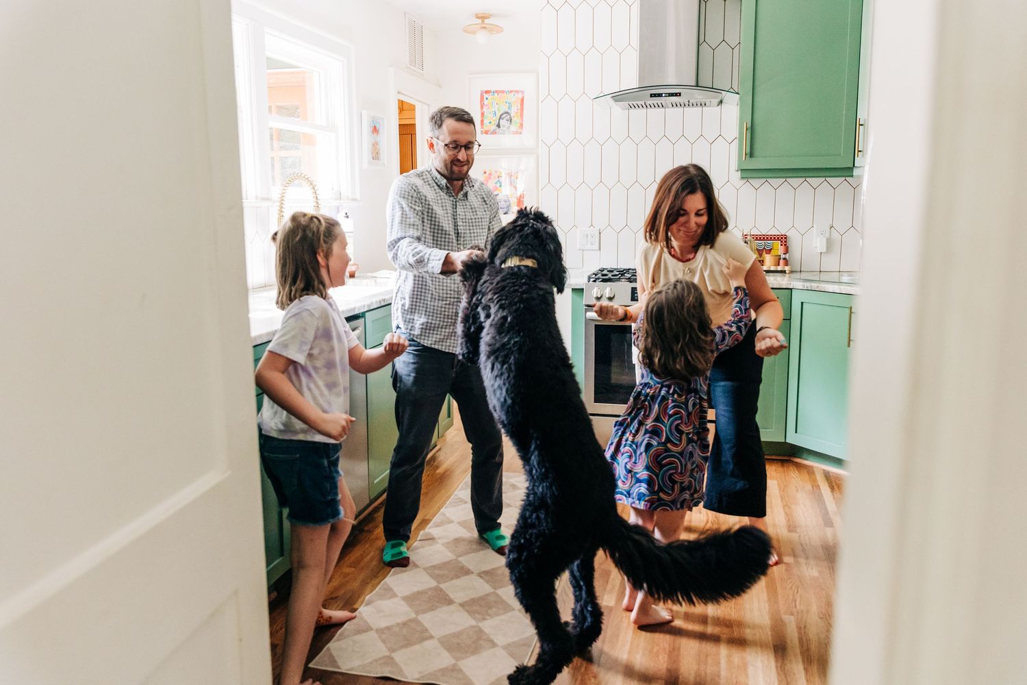 Family dances together and with their dog in their bright kitchen in Charlotte, NC. There are green cabinets.