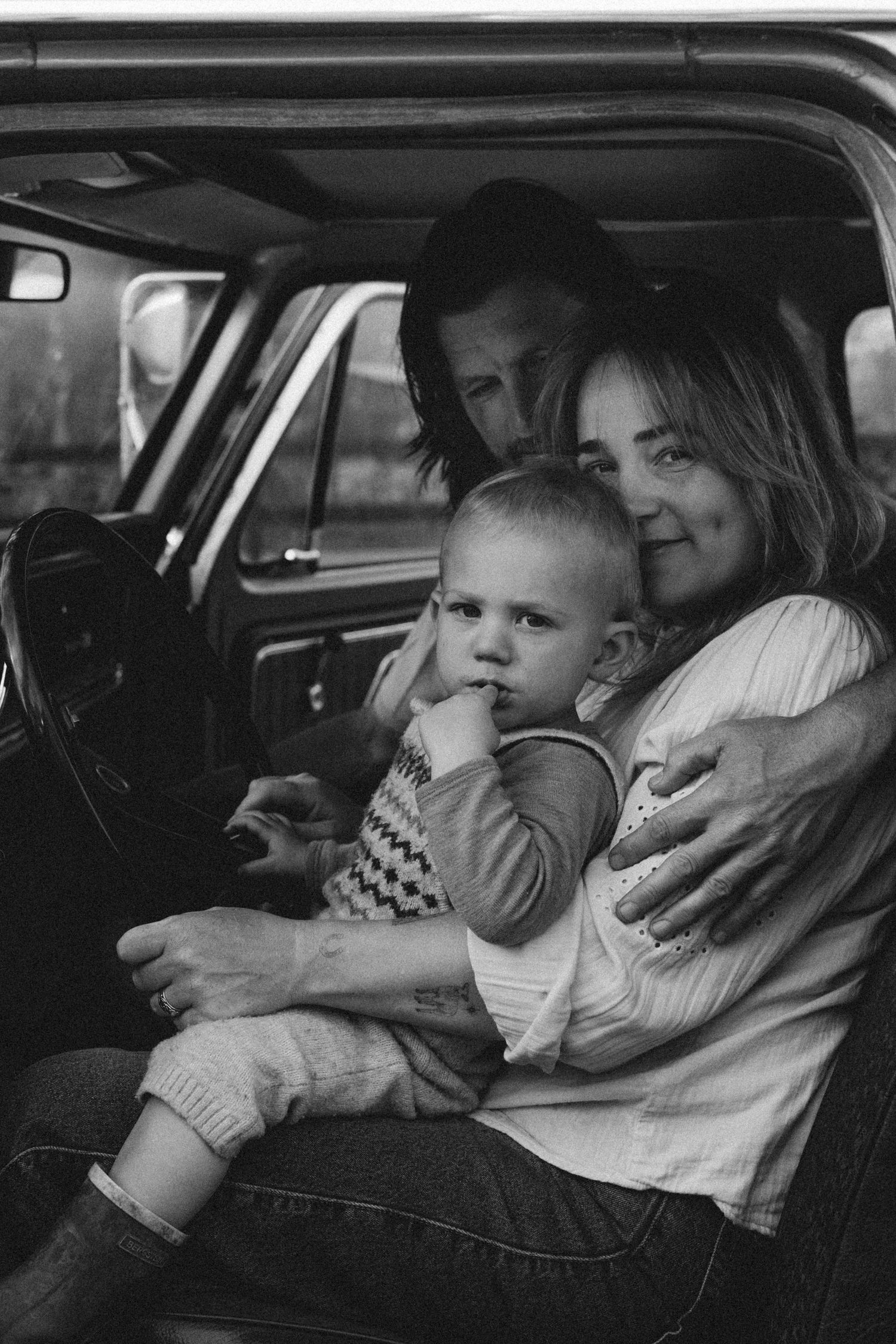 Black and white photo of a family with a baby sitting inside a vintage truck, mother and father embracing warmly Javea photographer