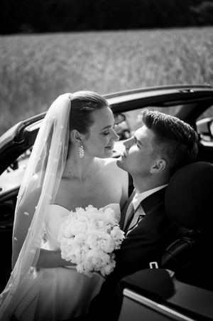 Cinematic Love: Elegantes Paar im Hochzeitsauto. Ein zeitloser Moment in Schwarz-Weiß, pur und voller Emotionen festgehalten. Fabio Marras