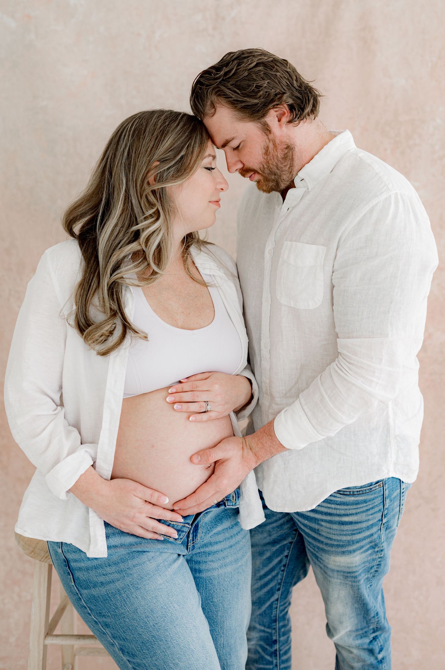 A a couple in white shirts and jeans against a neutral backdrop  answer the question "when is the best time to do a maternity shoot?"
