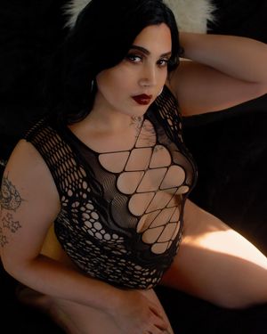 Person in black fishnet top posing seductively in dramatic lighting against dark background.