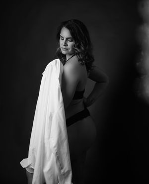 Black and white artistic portrait of a person in a white shirt against a dark background creating dramatic contrast.
