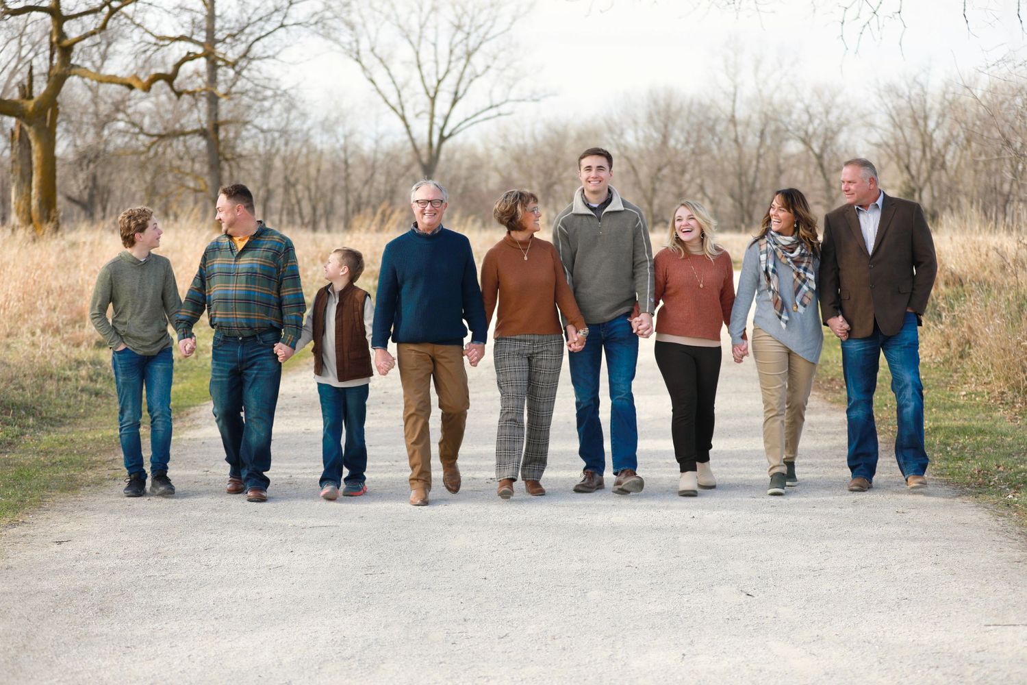 A multigenerational family walking together on a dirt path through a natural outdoor setting during autumn.
