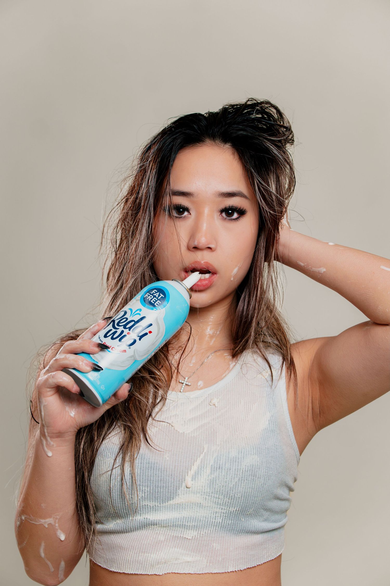A sequence of photos showing someone drinking from a blue beverage can while wearing a white top against a beige background.