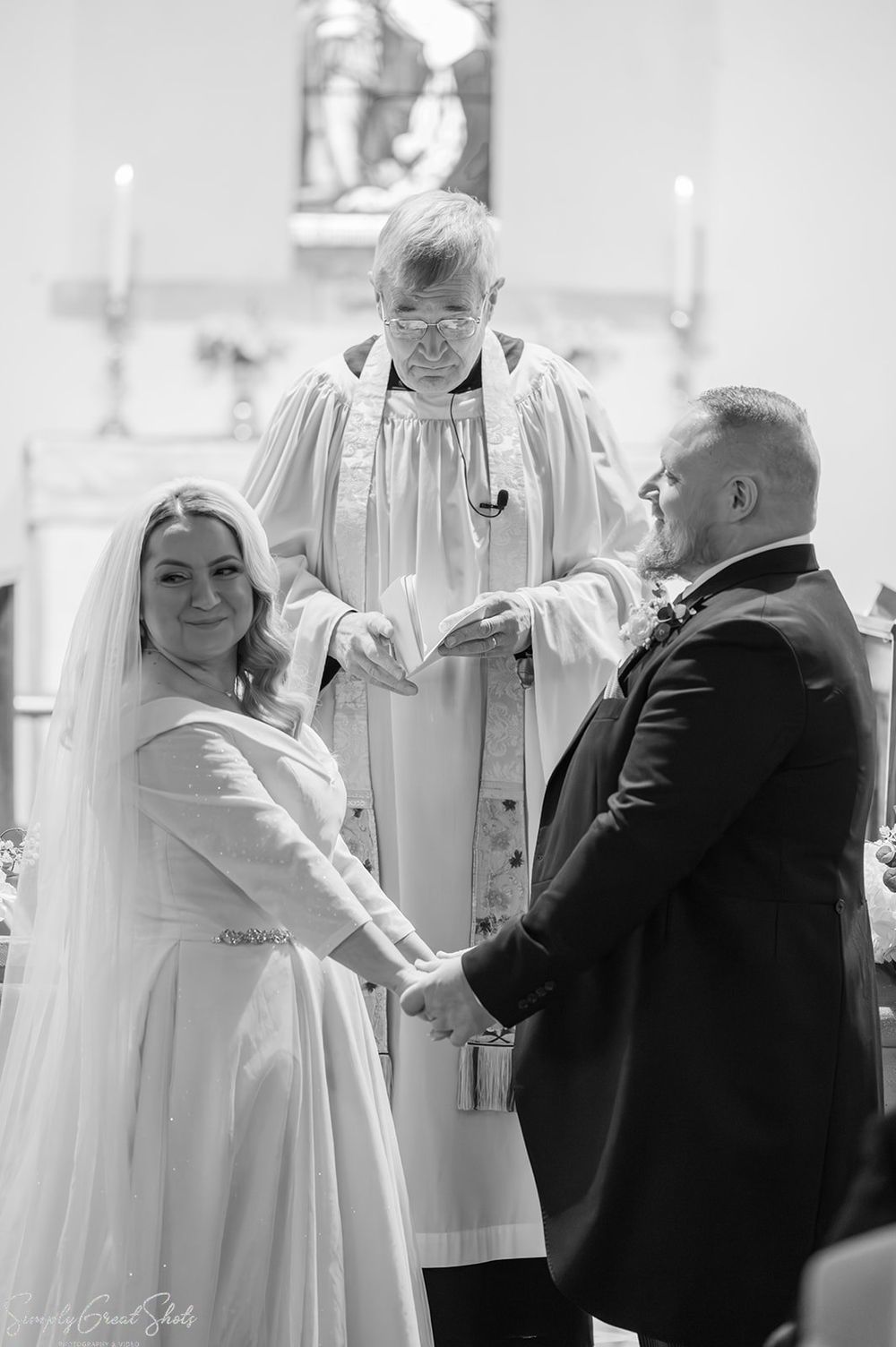 Black and white photograph of bride, groom and vicar during wedding ceremony at St Andrews Church Oxfordshire