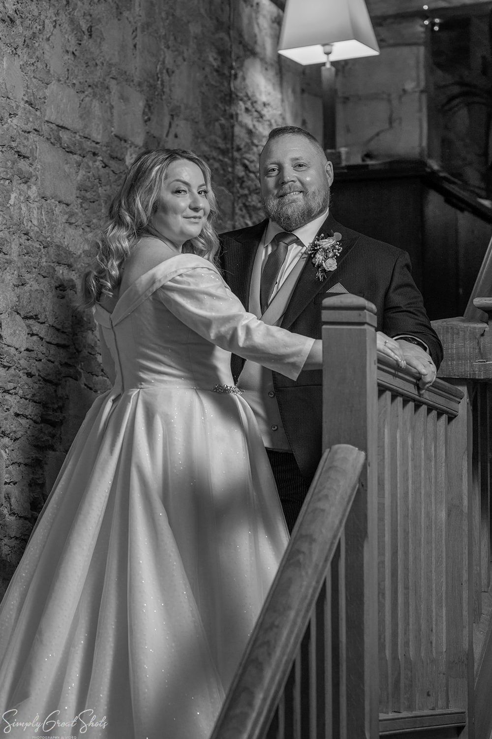 Black and white portrait of bride and groom on rustic wooden staircase with exposed stone walls at voco Oxford Thames