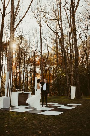 Bride and groom share first dance on black and white checkered outdoor dance floor at The Greenhouse at Arrows Farm in Lillington, NC.