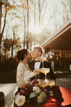 Newlyweds embrace romantically at sunset beside champagne tower with golden autumn trees in background.