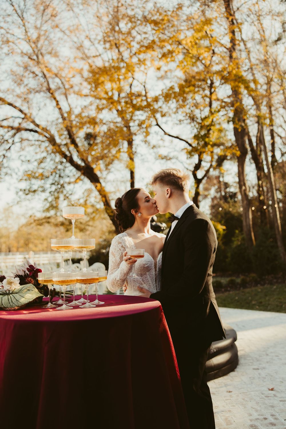 Bride and groom share a kiss beside champagne tower at outdoor autumn wedding reception table.