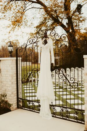Bride in long-sleeve lace wedding gown standing at ornate iron gates in autumn garden setting in Lillington, NC.