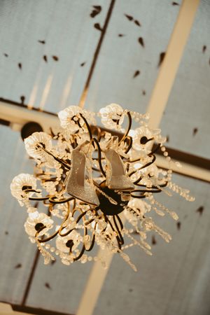 Bridal heels hanging elegantly from a crystal chandelier in a rustic venue ceiling.