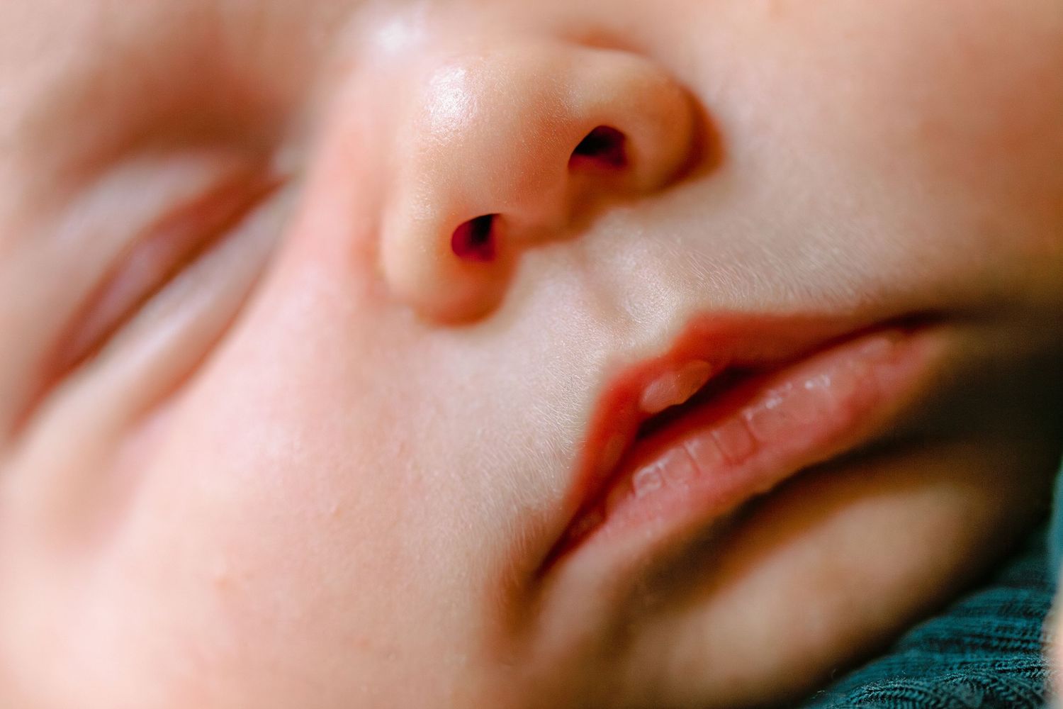 Extreme close-up macro photograph of lips and nose against turquoise background with soft focus effect.