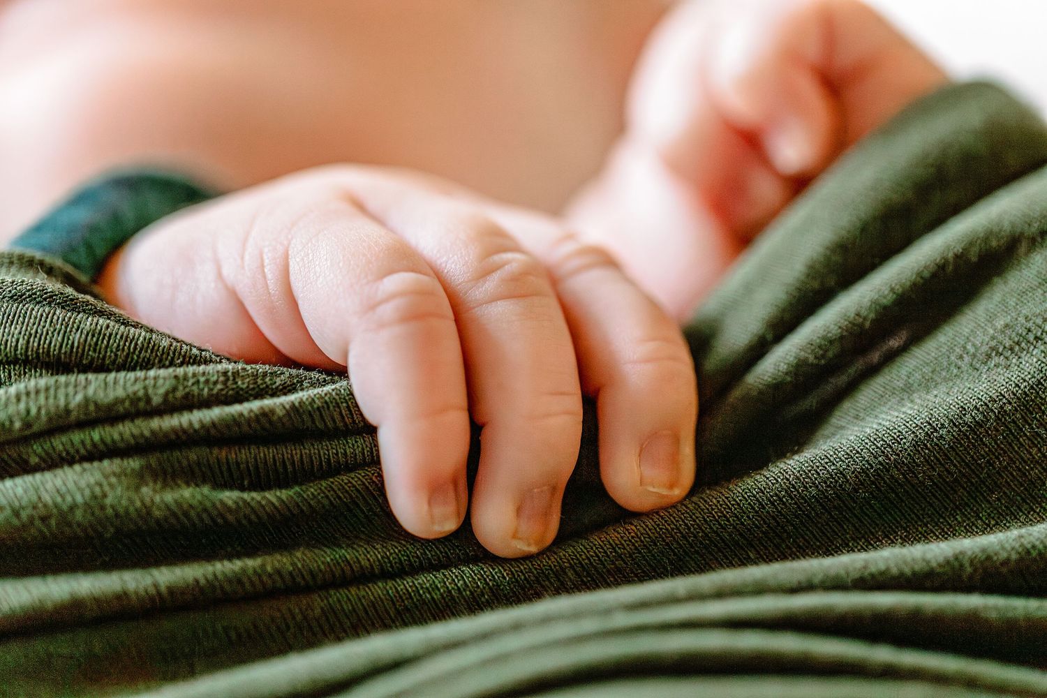 Small baby feet resting on dark green fabric with gentle natural lighting.