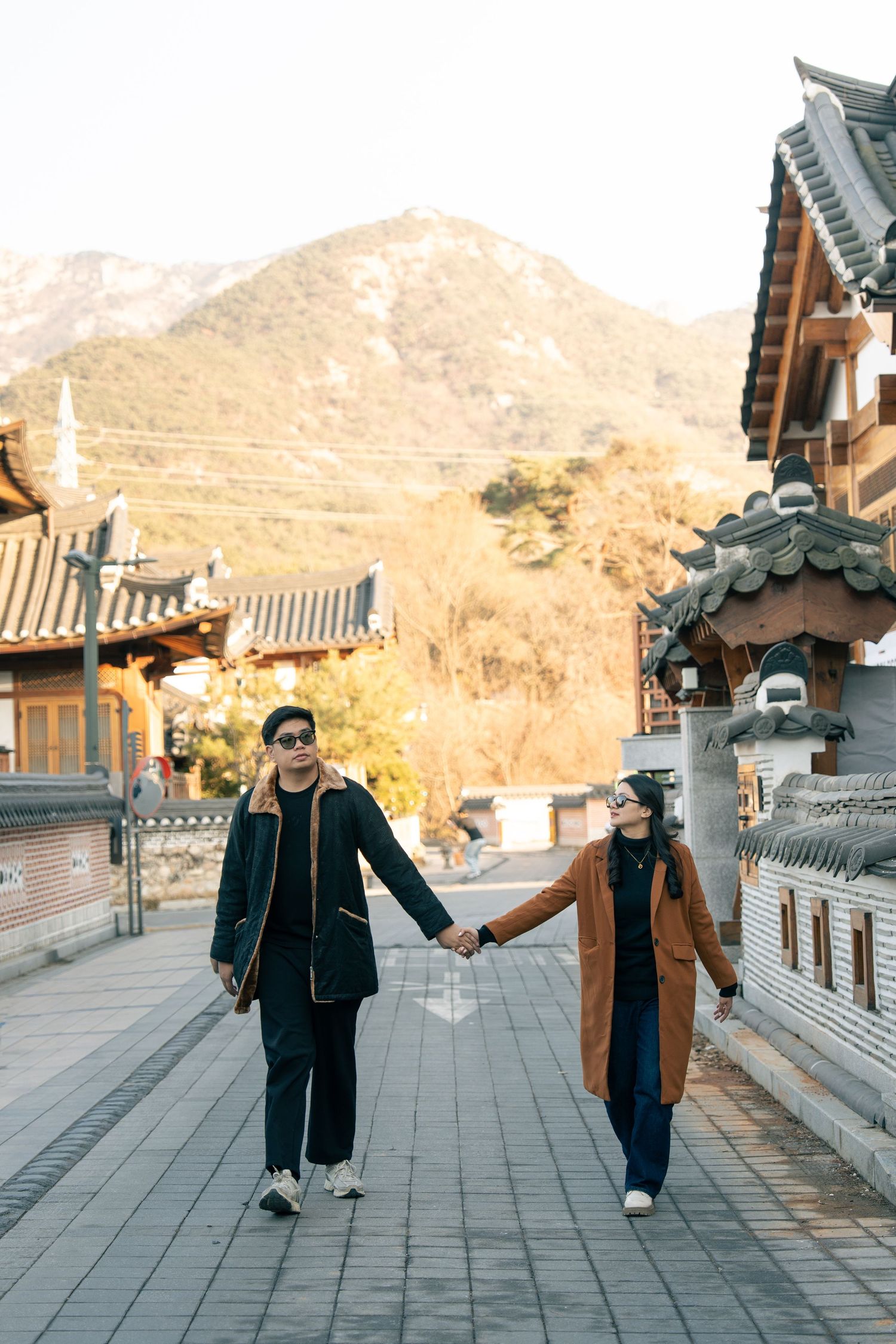 Two people walking together along a traditional Korean temple courtyard with mountains in the background.