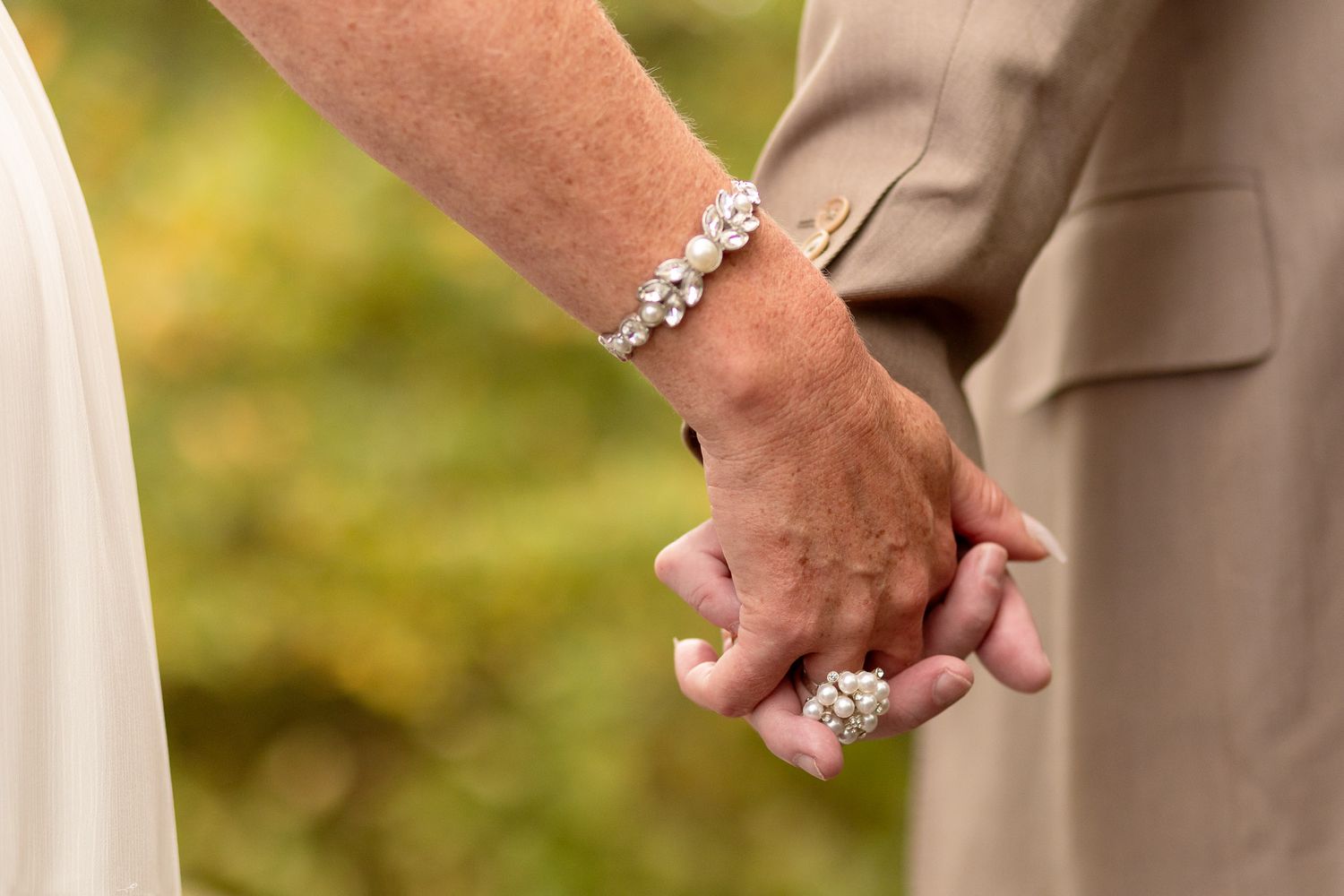 Close-up of two hands clasped together during a wedding ceremony, with a sparkly bracelet visible.