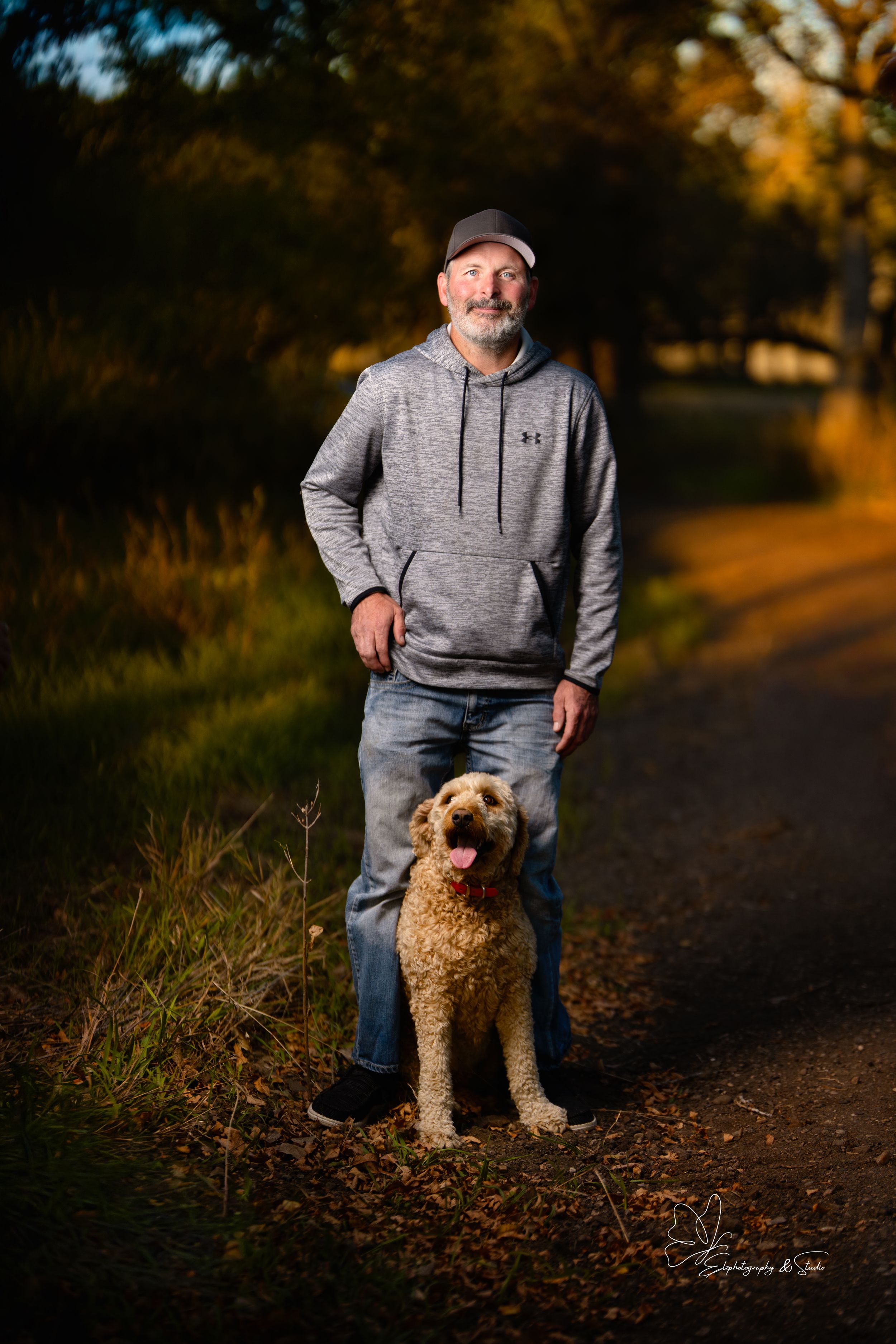 A person in a grey hoodie walks with their fluffy goldendoodle dog on an autumn path at sunset in Pierre, South Dakota.