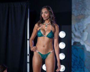 Fashion models showcase designer bikinis on a dark runway with dramatic lighting.