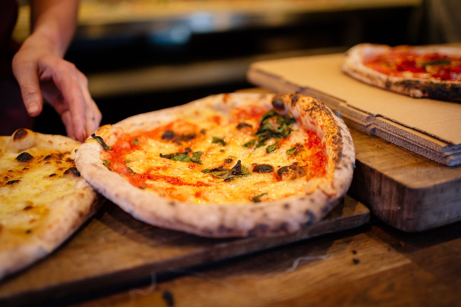 Fresh Neapolitan pizza with melted cheese and tomato sauce on wooden serving boards in restaurant setting.