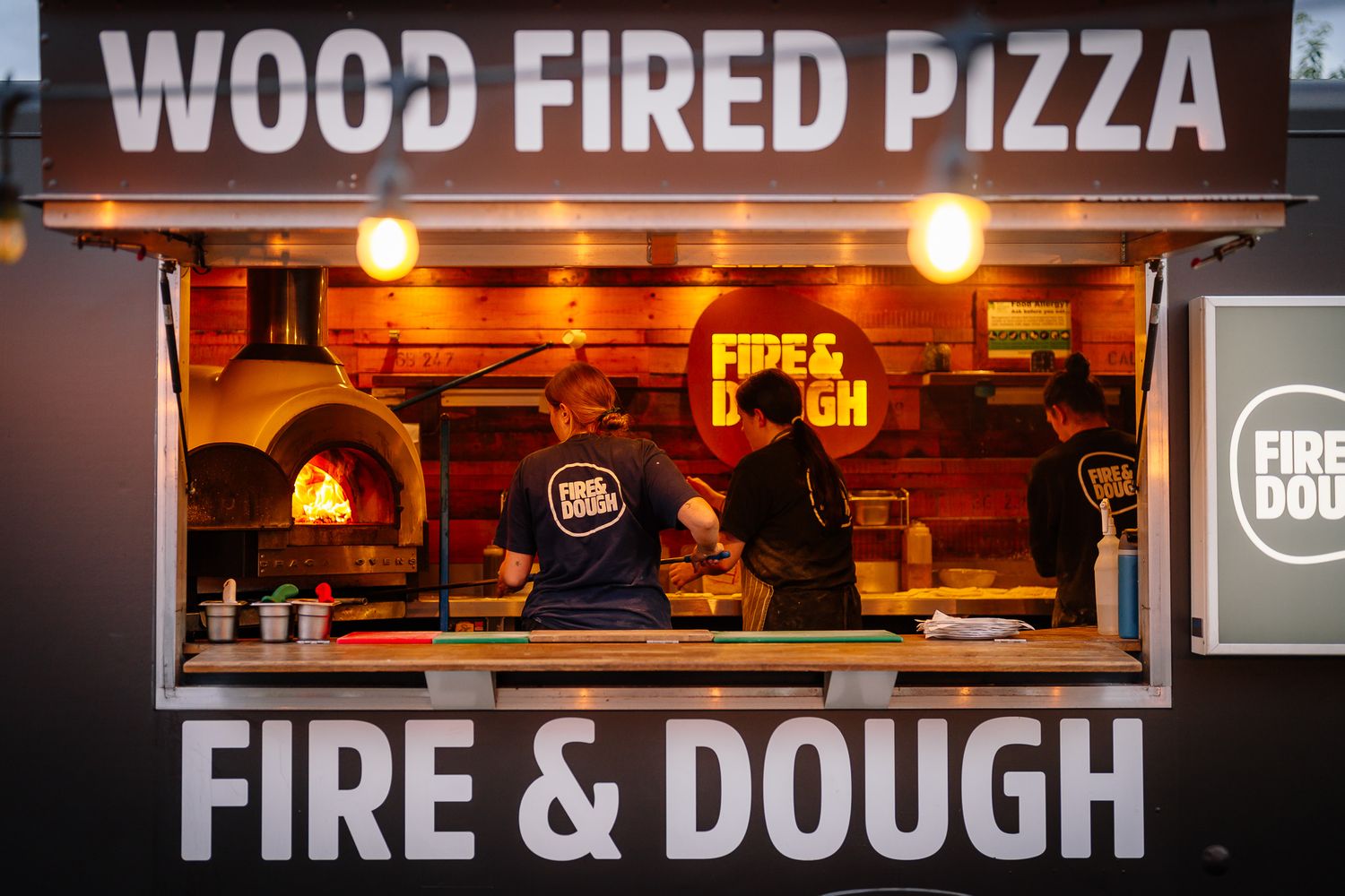 Wood fired pizza restaurant storefront with illuminated signage and warm lighting at night.