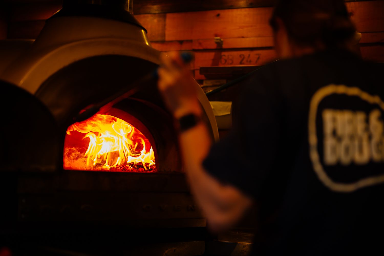 A glowing wood-fired pizza oven illuminates the dark with its bright orange flames inside the brick dome.