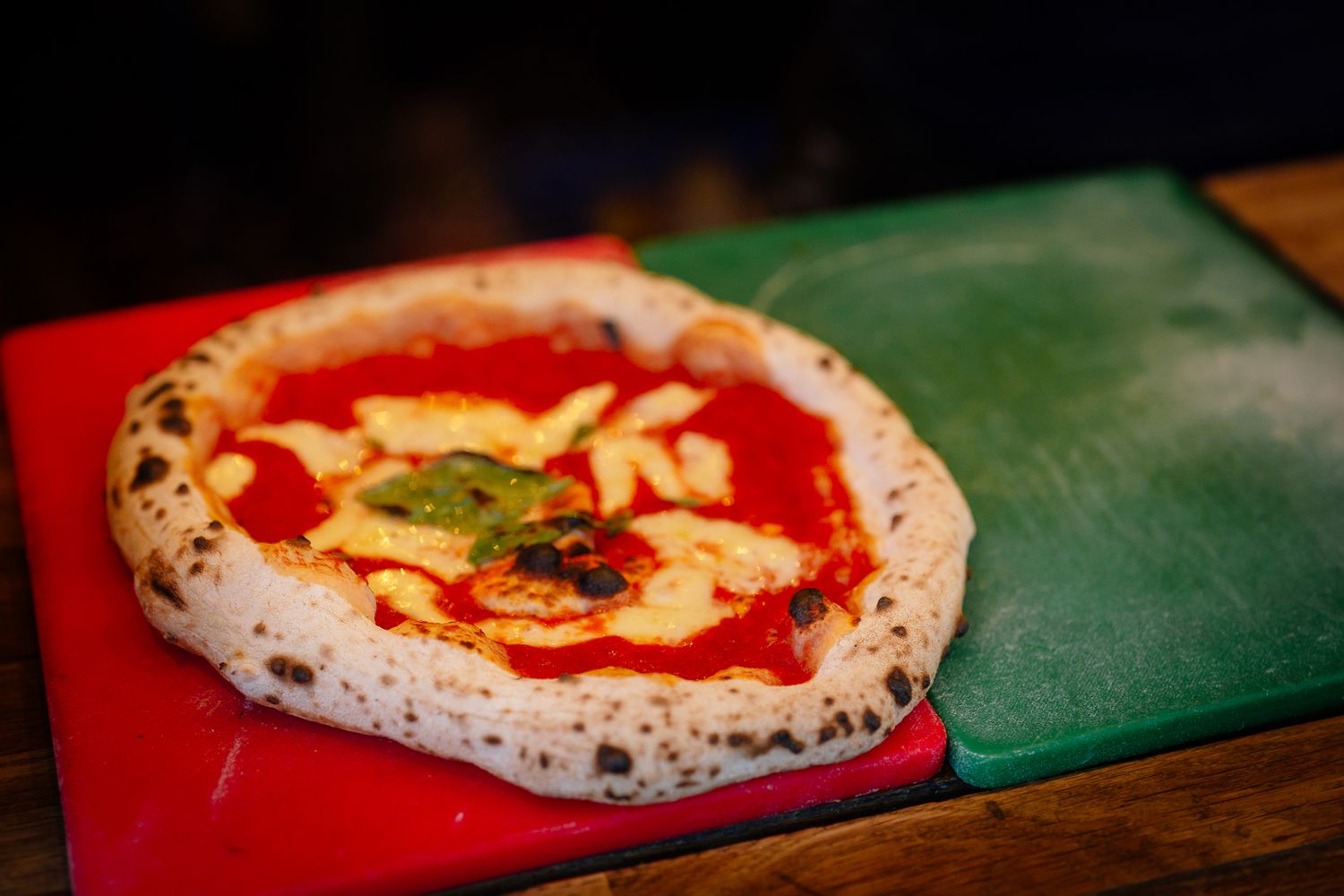 A traditional Neapolitan pizza with charred crust, tomato sauce, and melted cheese on a red and green serving board.