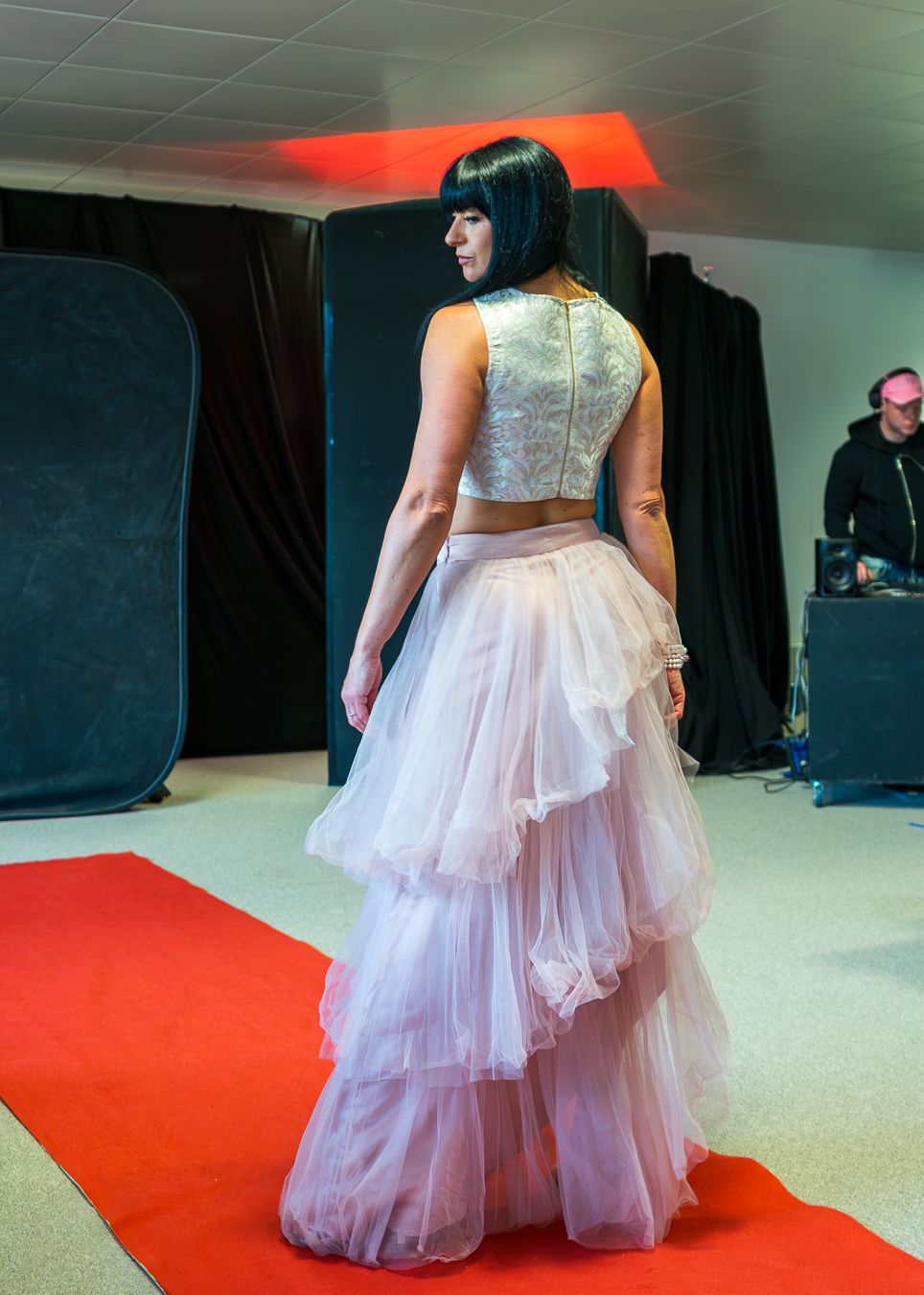 A person models a white tulle ball gown with a silver sequined bodice on a red carpet runway.